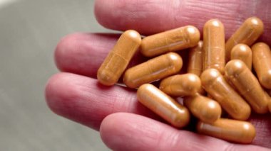 Doğal takvim çiçeği özütüyle yapılmış turuncu lutin kapsüllerini tutan elin yakın çekimi. Bitkisel ilaçlar.