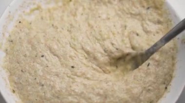 Çiğ hamuru bitki bazlı malzemelerle beyaz bir kasede karıştırmak. Eldeki kaşık kremalı hamuru karıştırıyor. Kapatın. Vejetaryen yemek konsepti