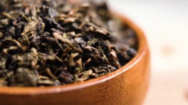 Kurumuş yeşil barut çay yaprağı topakları ağır çekimde ahşap bir konteynırın üzerine düşüyor. Kuru aromatik bitki yaprakları. Çin içeceği. Makro