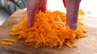 Tahta kesme tahtasının üzerinde parçalanmış balkabağını tutan el. Parlak turuncu doku. Bulanık metal rendesi. Pişirme hazırlığı ve vegan sebze yemeği konsepti