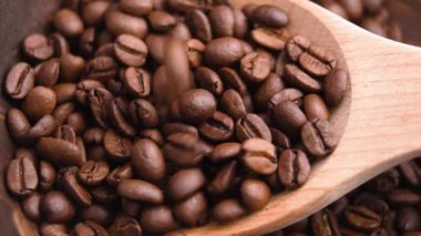 Rustik tahta kaşık organik kavrulmuş kahve çekirdekleri ile dolup taşıyor. Gurme ilham kaynağıdır. Ağır çekim. Üst Manzara. Makro çekim