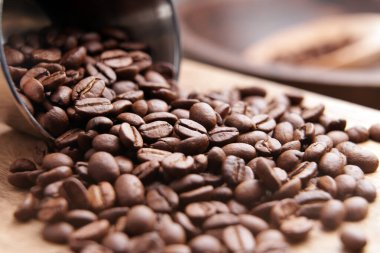 Yeni kavrulmuş arabika kahve çekirdekleri mutfak ortamında bir çelik bardağa saçılmış. Makro