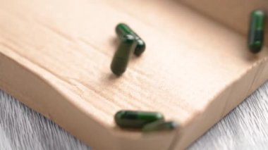 Bitki özlerinin bulunduğu yeşil bitkisel kapsüller ahşap yüzeyde bir karton kutunun içine düşüyorlar. Organik destek ambalajı. Yakın plan.