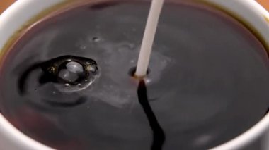 Bir fincan sıcak sade kahveye taze süt dökülüyor. Beyaz kremalı girdap ve koyu kahve karışımı. Canlandırıcı aromatik sabah içeceği hazırlığı. Makro çekim