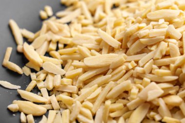 Dilimlenmiş bademler siyah bir tabağa saçılmış. Pişirme ve pişirme malzemeleri, besin değeri yüksek. Organik çiğ fındık. Yakın plan.