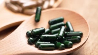 Tahta bir kaşığa düşen yeşil bitkisel kapsüller. Alternatif tıp konsepti. Yavaş çekim