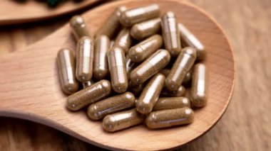 Kahverengi bitkisel kapsüller tahta kaşıkta. Doğal bitkisel ilaçlar. Yakın plan çekim. Üst Manzara. Döndürme