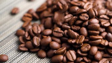 Koyu kavrulmuş kahve çekirdekleri yavaş çekimde dokunmuş bambu bir mutfak paspasının üzerine düşüyor. Organik Arap tanecikleri