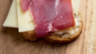 Emmental peynirli ve İspanyol jamonlu taze sandviç ve tam buğday ekmeği dilimi. Ahşap arka plan. Üst görünüm. Döndürme