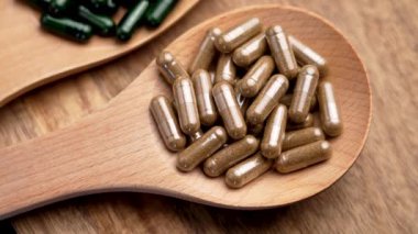 Kırsal arka planda farklı bitkisel kapsüllere sahip tahta kaşıklar. Alternatif ilaç takviyeleri. Üst Manzara. Döndürme