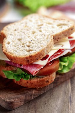 Haşlanmış jambonlu tam tahıllı sandviç, Kumato domatesi, İsviçre peyniri ve ahşap tahtada taze marul.