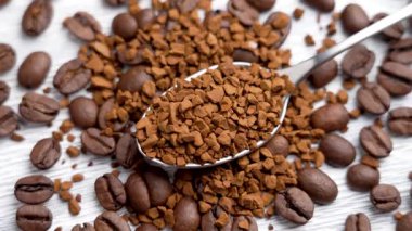 Metal kaşıkla granüle edilmiş hazır kahve ve beyaz tahtanın üzerinde kavrulmuş Arap fasulyesi. Üst Manzara. Döndürme