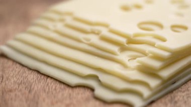 Tahta yüzeyinde yuvarlak delikleri olan ince İsviçre peyniri dilimleri yığını. Organik süt ürünü. Yakın plan çekim. Döndürme