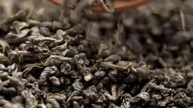 Tahta kaşıktan dökülen sarılmış Çin yeşil çay yaprakları. Geleneksel içecek malzemesi. Makro çekim