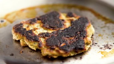 Kavrulmuş bir yüzeyi olan paslanmaz bir kızartma tavasında yanmış börek. Ön manzara. Kapatın. Döndürme