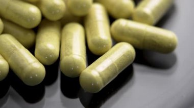 Siyah cam yüzeyde sarı yeşil ilaç kapsülleri. Doğal diyet takviyeleri. Makro. Döndürme