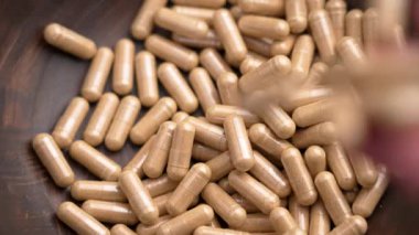 Besin özü içeren destek kapsülleri yavaş çekimde elden ahşap kaseye düşüyor.