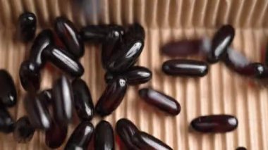 Koyu kırmızı yarı şeffaf Omega 3 kapsülleri karton kutuya dökülüyor. Beslenme hapları paketliyorum. Yavaş çekim