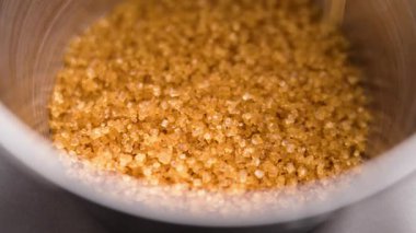 Kahverengi kamış şeker kristalleri ağır çekimde metal bir kabın içine düşüyor.