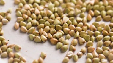 Çiğ karabuğday taneleri seramik yüzeye yavaş çekimde düşüyor. Pişmemiş aşçılık malzemeleri. Makro çekim