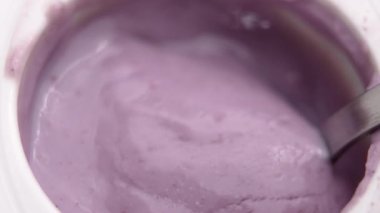 Çay kaşığı, beyaz plastik bir kabın içinden yabanmersinli süt yoğurdu topluyor. Taze besin ürünleri ve böğürtlen malzemeleri. Makro çekim