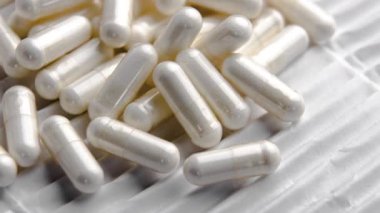 Beyaz kıvrımlı kağıt üzerinde dönen makro ilaç kapsülleri.