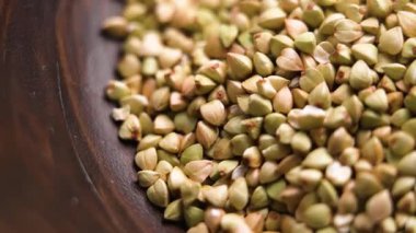 Pişmemiş yeşil karabuğday taneleri yavaş çekimde ahşap bir kaseye düşüyor. Kurutulmuş beslenme malzemesi. Makro atış. Döndürme