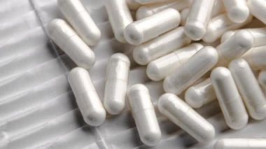 Beyaz ilaç kapsülleri tırtıklı ambalaj kağıdı yüzeyine saçılmış. Makro atış. Döndürme