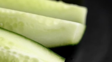 Çiftliğin taze organik salatalık parçaları siyah bir seramik tabakta uzunlamasına dilimlenmiş. Döndürme