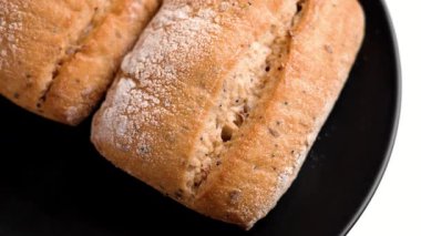 Taze pişmiş ekmek ruloları, siyah seramik tabakta altın çatlamış kabuk ve bir çörek alan el.