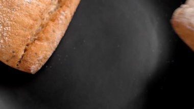 Taze ekmek rulosu siyah bir seramik tabağa elle yerleştirilir. Fırında buğday ekmeği. Üst görünüm