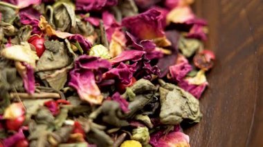 Ahşap bir kasede, ambar yaprakları ve papatya çiçekleri ile karışık malzemeli yeşil çay. Makro atış. Döndürme