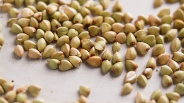 Tabağa saçılmış pişmemiş yeşil karabuğday taneleri. Makro atış. Döndürme