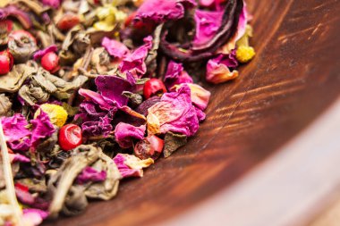 Ahşap bir kasede, ambar yaprakları ve papatya çiçekleri ile karışık malzemeli yeşil çay. Makro çekim. 