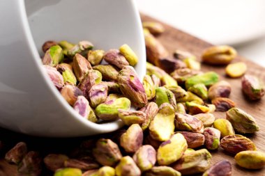 Soyulmuş şam fıstığı çekirdekleri içinde beyaz seramik bardak ahşap masa üzerine serpiştirilmiş.