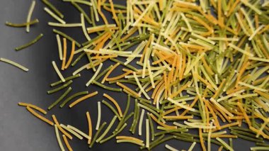 Siyah seramik yüzeyde ince renkli vermicelli. Akdeniz diyetinin pişmemiş kuru malzemesi. Üst Manzara. Döndürme