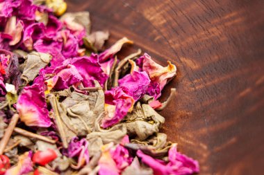 Kurumuş yeşil çay yaprakları ve ahşap bir kasede gül yaprakları olan malzemeler için.