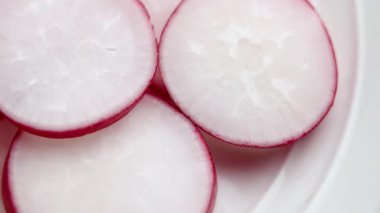 Mavi kenarlı, beyaz seramik tabakta taze dilimlenmiş turplar. Çiğ salata, besleyici malzeme. Makro atış. Döndürme