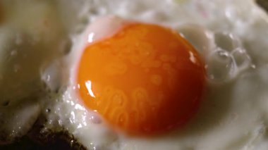Mutfak ocağında tavada yumurta pişirmek. Yakın çekim. Geleneksel sabah kahvaltısı hazırlanıyor.