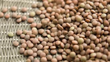 Çiğ mercimek taneleri yeşil hasır yüzeyde yavaş çekimde düşüyor.