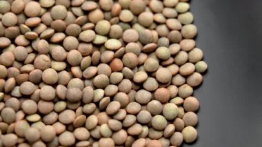 Siyah seramik üzerinde pişmemiş organik mercimek taneleri. Yakın plan. Döndürme. Üst görünüm