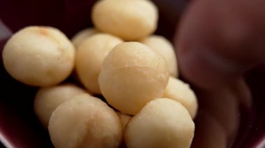 Kavrulmuş macadamia meyveleri ve kırmızı seramik kaseden somun somunu alıyor.