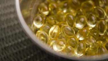 Vitamin D3 softgel kapsülleri ağır çekimde metalik bir kaba düşüyor. Sarı diyet takviyeleri. Makro