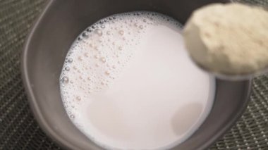 Bir kase bitki bazlı badem sütüne kaşık protein tozu ekliyorum. Besleyici diyet içeceği yapıyorum. Yakın plan. Üst görünüm