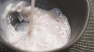 Bitki bazlı badem sütü yavaş çekimde gri kaseye dökülüyor. Beslenme içeceği.