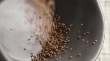 Besleyici besin değeri yüksek glütensiz karabuğday taneleri yavaş çekimde gri kaseye dökülüyor.