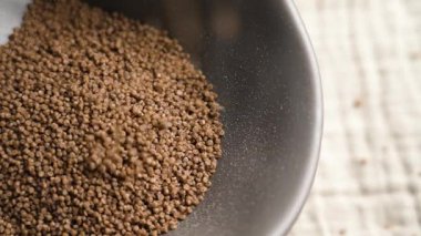Pişmemiş karabuğday kuskuskusunu gri mutfak kâsesine yavaş çekimde kumaş masa örtüsüne döküyorum. Beslenme malzemesi