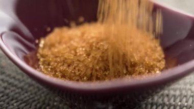 Kahverengi şeker kristalleri yavaş çekimde kırmızı seramik kaseye dökülüyor.