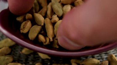 Aromatik kardamon kapsülleri ve el kırmızı seramik kaseden Asya baharatı topluyor.