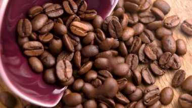Kavrulmuş kahve çekirdekleri, ahşap masadaki kırmızı kaseden dökülen Arap taneciklerinin üzerine ağır çekimde düşüyor.